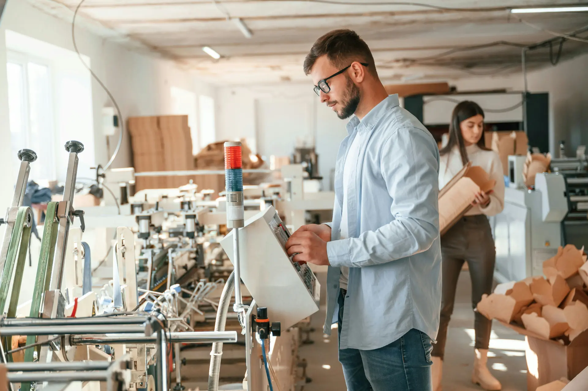 Hombre con gafas revisando paquetes con un escáner en las estanterías de una nave industrial.