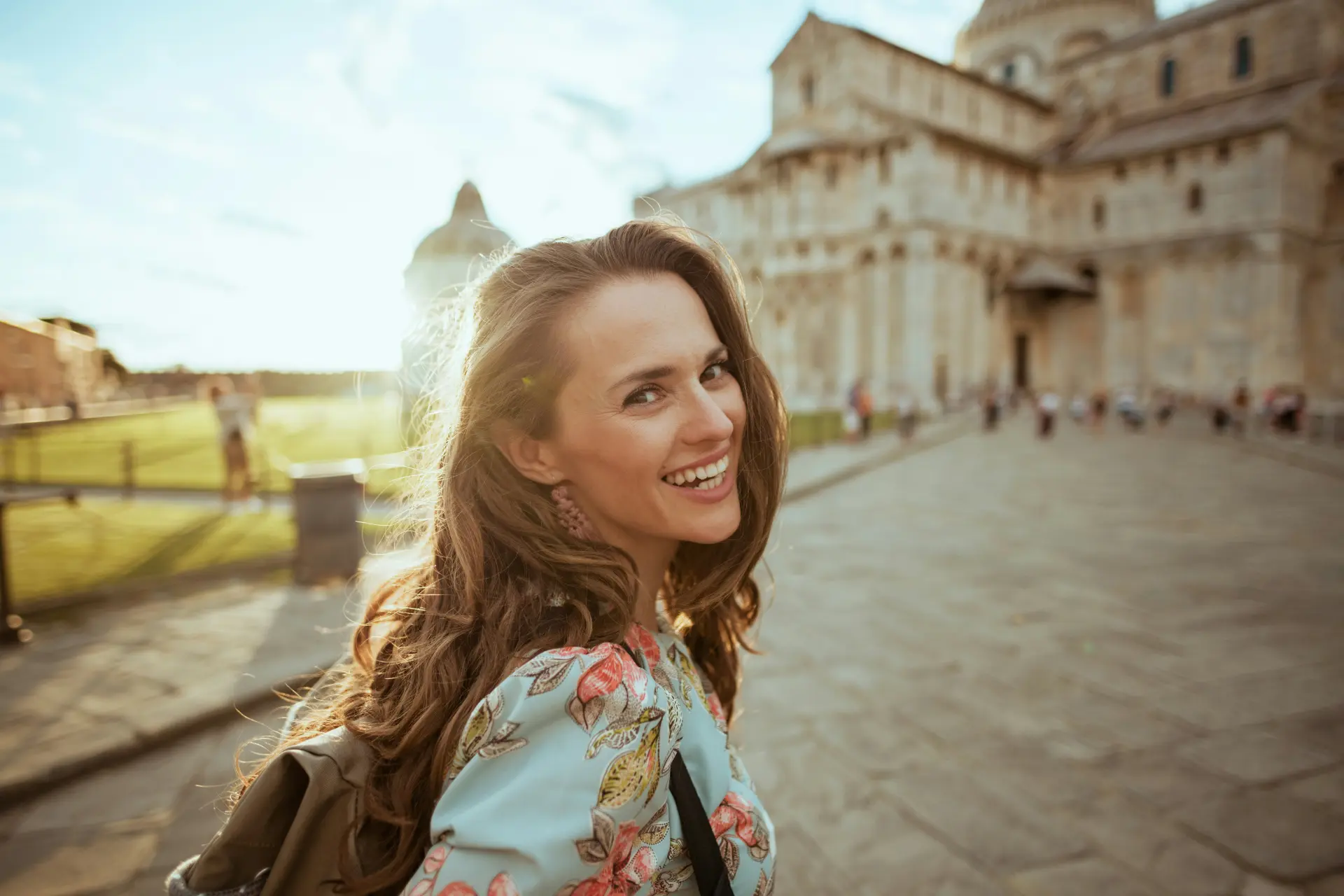 Turista joven sonriendo frente a una catedral histórica iluminada por el sol.